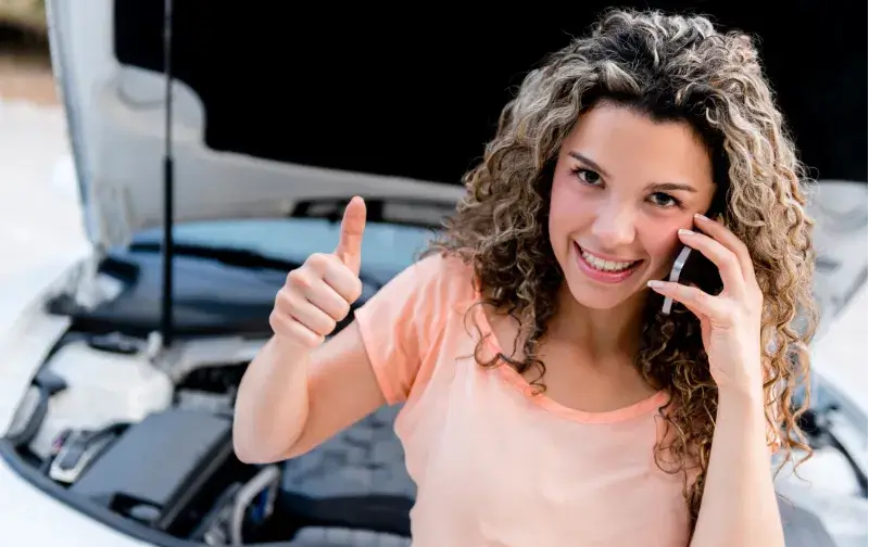 Motorista ao telefone ao lado do carro com o capô aberto. Imagem ilustrativa.